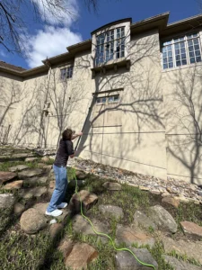 Window Cleaning Kansas City. Person using a long pole to clean second-story windows on a large beige house.