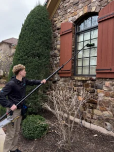 professional window cleaner using an extendable tool for second-story windows on a stone house in kansas city